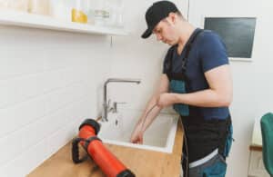 Professional drain cleaning technician clearing a stubborn clog from a residential kitchen sink using an electric drain auger.